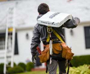 Roofer carrying shingles, climbing ladder to house.