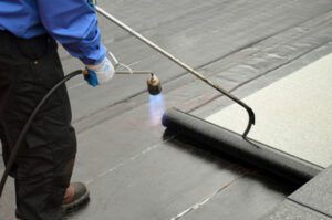 Worker applying waterproofing membrane on roof with torch