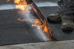 Worker applying torch-applied roofing material with fire.