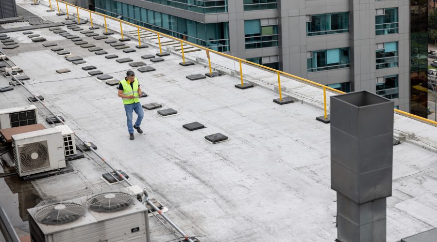 Roof maintenance engineer doing a routine inspection on the rooftop of a building and taking notes on his tablet