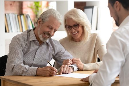 Smiling couple signing paperwork with advisor.