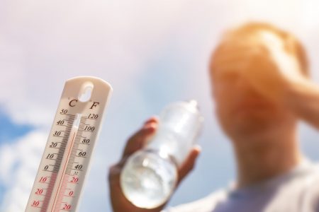 Person holding water bottle near hot thermometer.