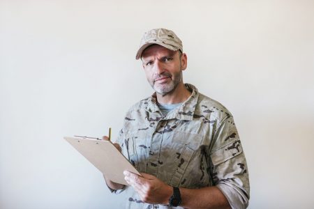Military person with clipboard in desert uniform.